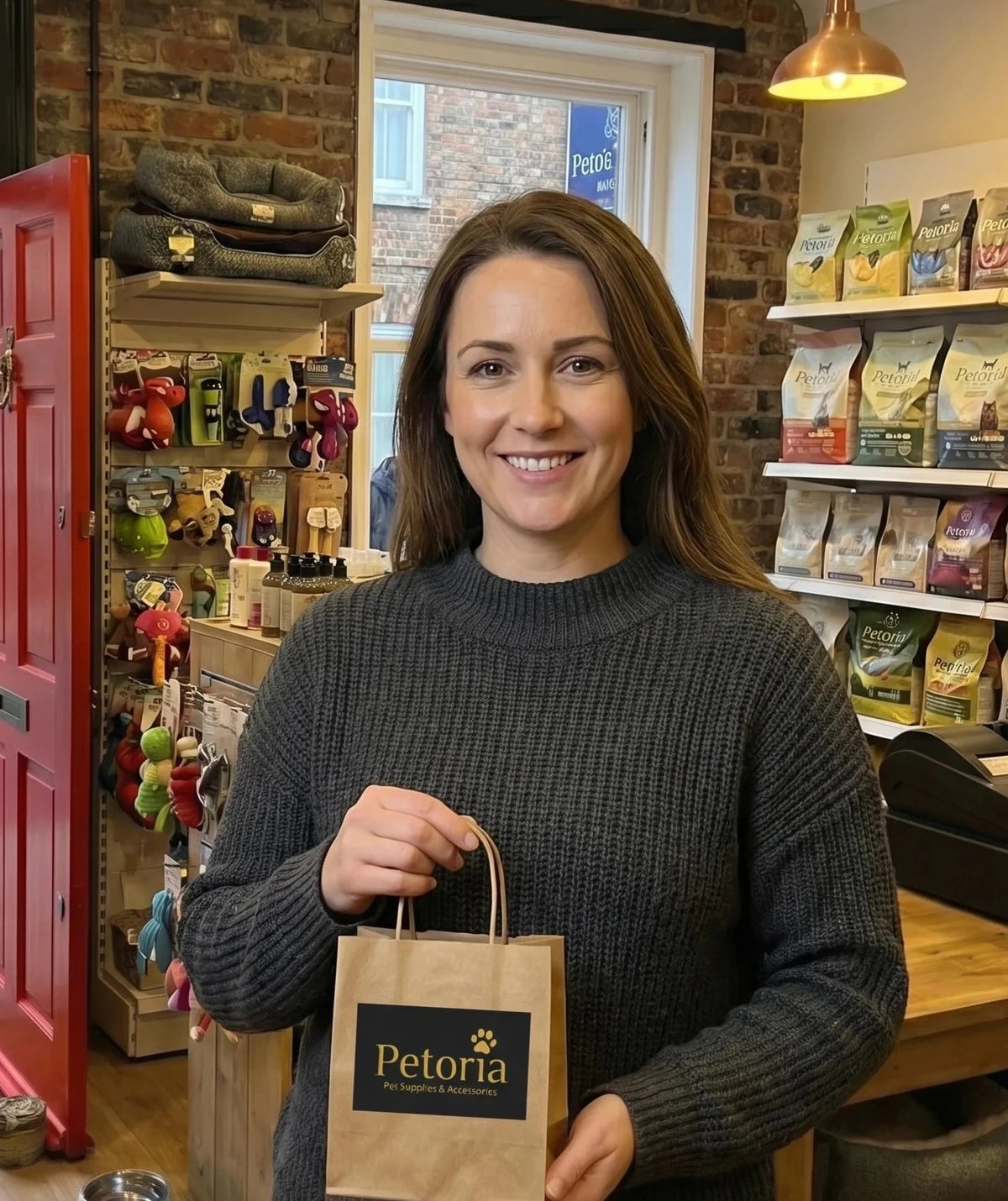 Woman holding a brown paper bag with 'Petoria' branding in a pet store.